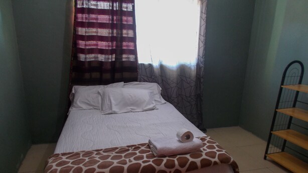 Un lit avec une couvre-lit à motifs de girafe, un oreiller blanc et une serviette enroulée posée sur le côté.