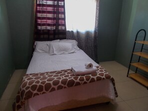 A bed with a giraffe-patterned bedspread, a white pillow, and a rolled-up towel on the side. - Shantumbu Lodge (Lusaka)