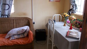 Une pièce comprenant un canapé en osier, une table à manger avec des chaises, un calendrier et une fenêtre avec des rideaux.