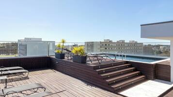 Una terraza en la azotea con suelo de madera, una piscina y plantas en macetas.