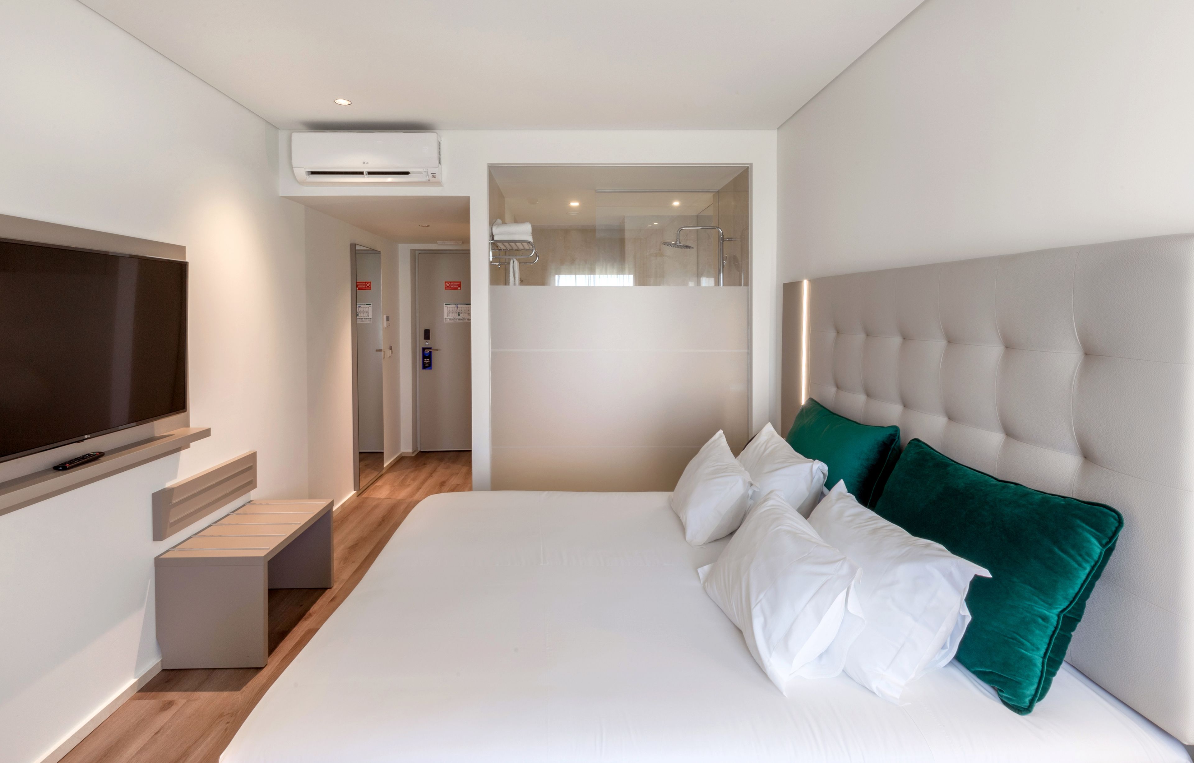 Ein modernes Hotelzimmer mit einem großen Bett, einem Flachbildfernseher, einer Klimaanlage und Blick ins Bad.