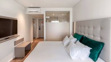 A modern hotel room with a large bed, a flat-screen TV, a built-in air conditioning unit, and a view of the bathroom.