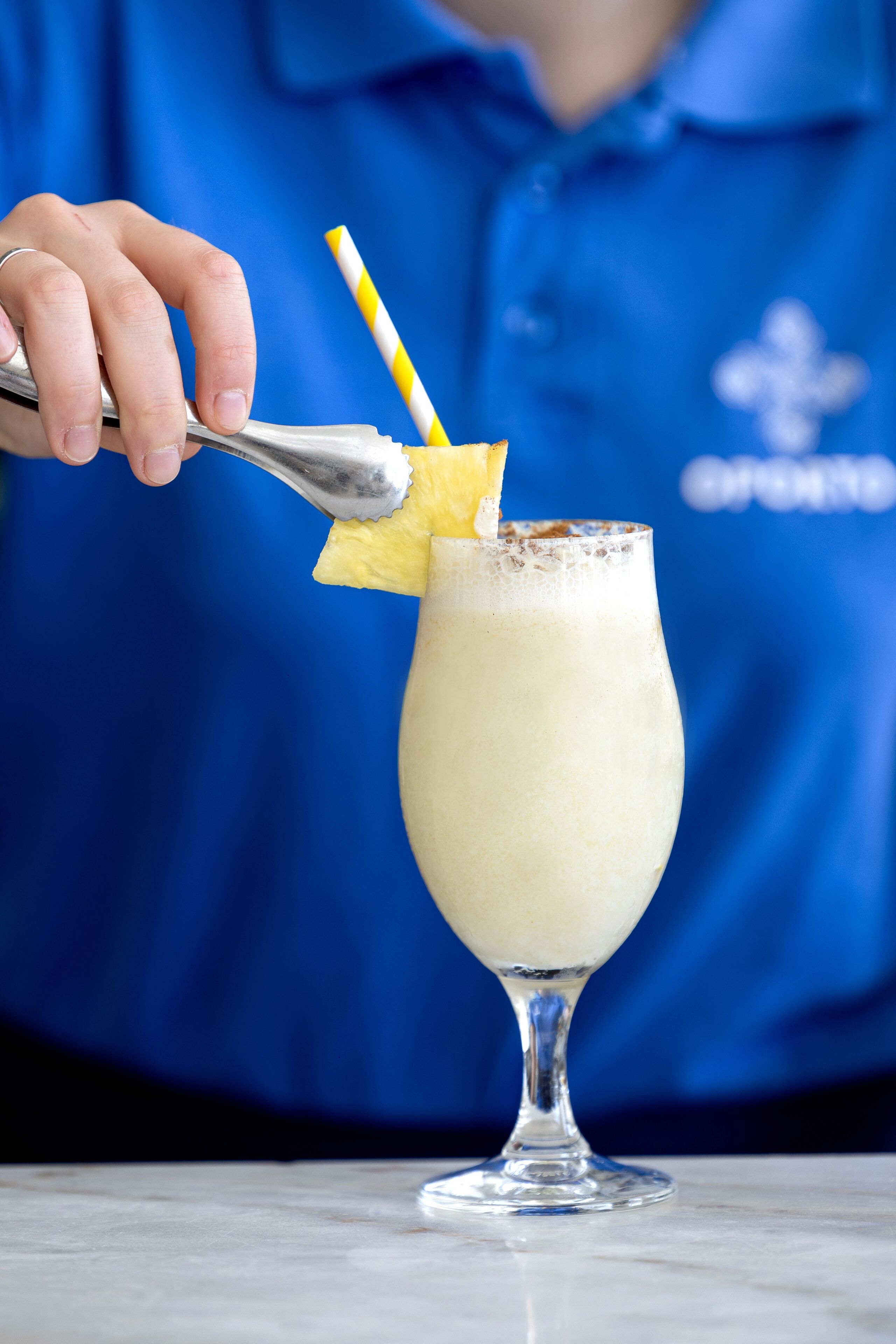 Una persona con una camisa azul preparando una bebida con una cuchara y una pajita rayada de amarillo y blanco.
