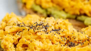 A close-up of scrambled eggs on toast with avocado and black sesame seeds.