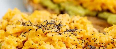 A close-up of scrambled eggs on toast with avocado and black sesame seeds.