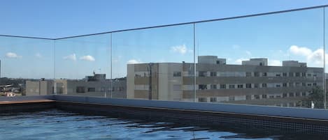 Una piscina en la azotea con agua cristalina, rodeada por una barandilla de vidrio.