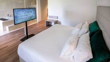 A modern hotel room with a large bed, a flat-screen TV, a bathroom with a bathtub, and a walk-in closet.