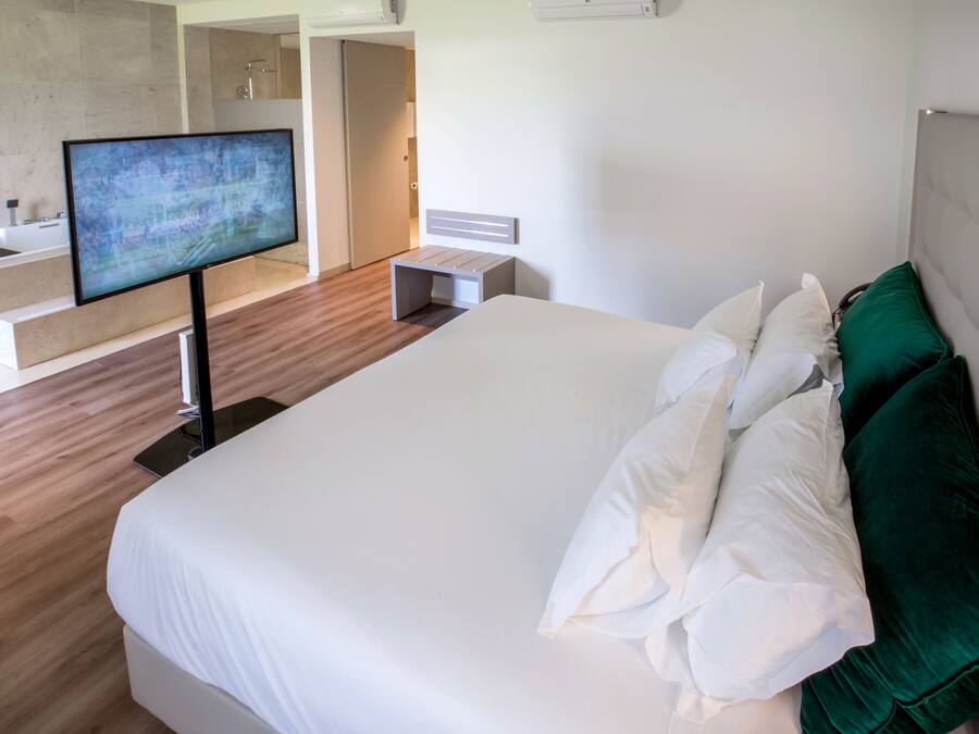 A modern hotel room with a large bed, a flat-screen TV, a bathroom with a bathtub, and a walk-in closet.