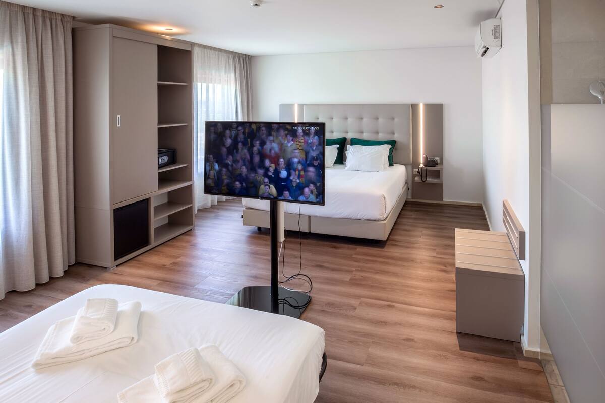 Hotellihuone, jossa on sänky, televisio, vaatekaappi ja yöpöytä.