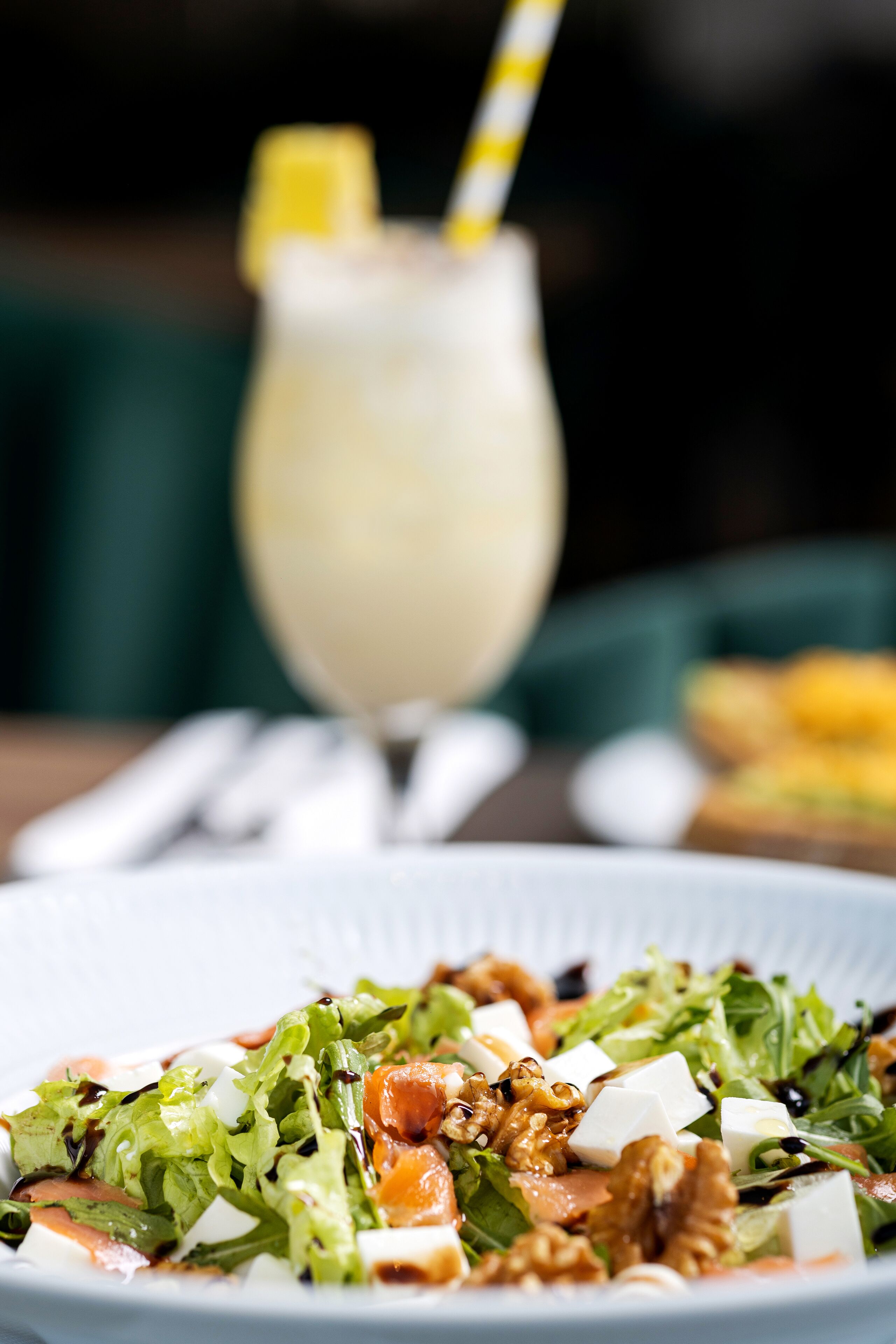 Un piatto di insalata con noci e formaggio, un bicchiere di bevanda con una fetta di limone e una cannuccia a righe.