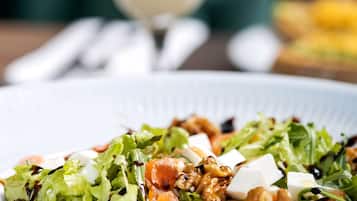 Un piatto di insalata con noci e formaggio, un bicchiere di bevanda con una fetta di limone e una cannuccia a righe.