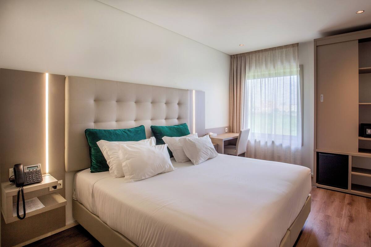 Hotellihuone, jossa on suuri sänky, puhelin sängyn vieressä, työpöytä ja vaatekaappi.
