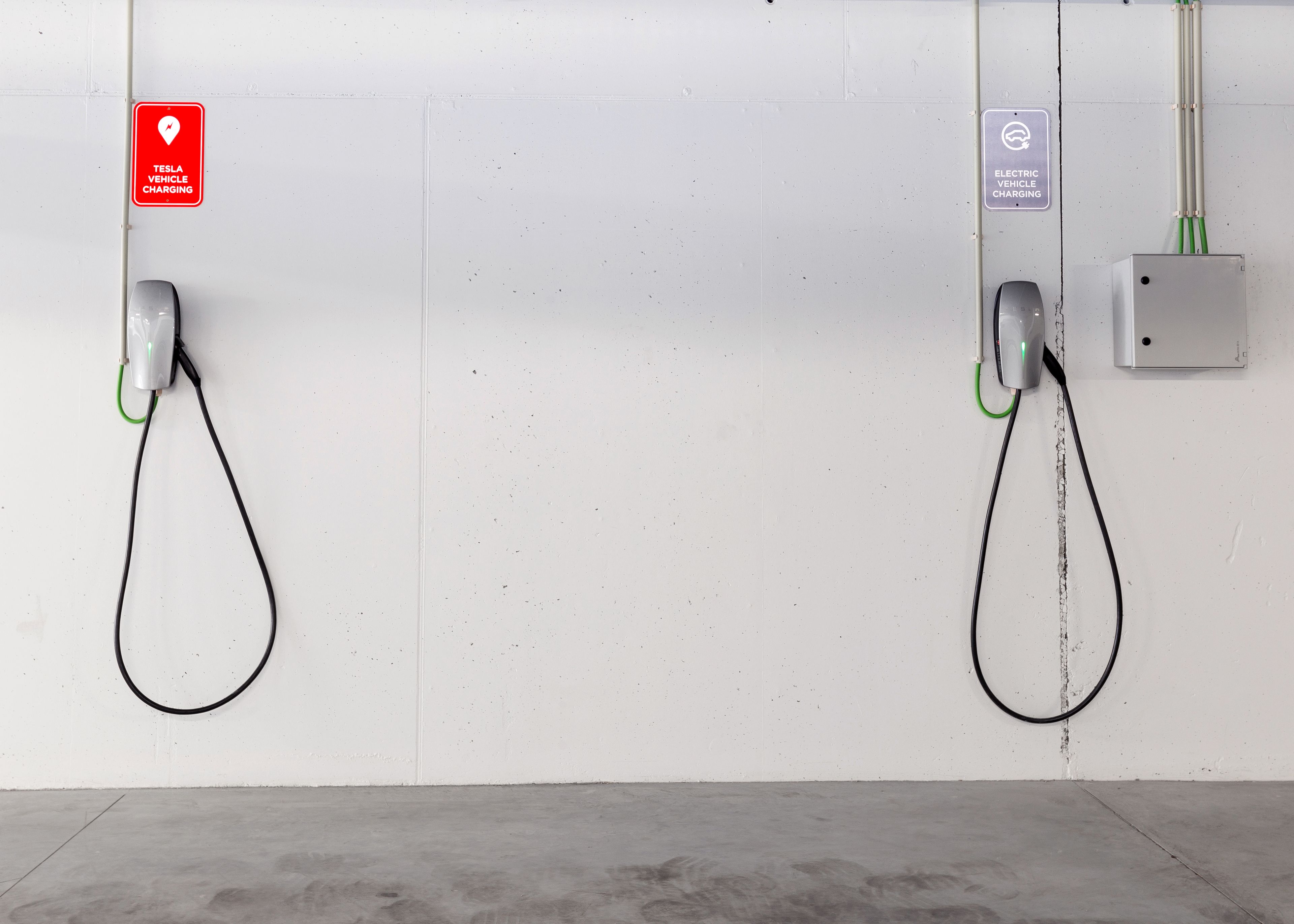 Two electric vehicle charging stations mounted on a white wall with a concrete floor.