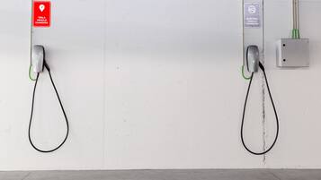 Two electric vehicle charging stations mounted on a white wall with a concrete floor.