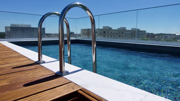 Una piscina en la azotea con agua azul cristalina, barandillas de metal y una cubierta de madera.