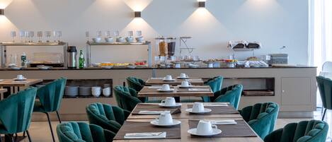 A modern dining area with teal chairs and tables, a buffet with various food items, and a coffee station.