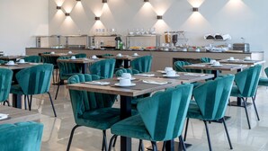 Un comedor moderno con sillas tapizadas en color verde azulado y mesas, equipado con diversos productos para el desayuno y una estación de café.