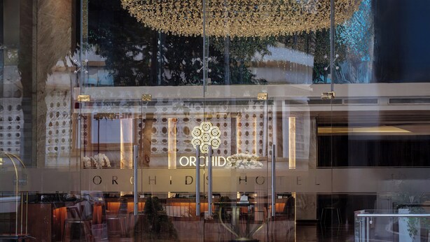 L’extérieur de l’hôtel Orchid présente un design moderne, avec une grande façade en verre et un logo bien visible.