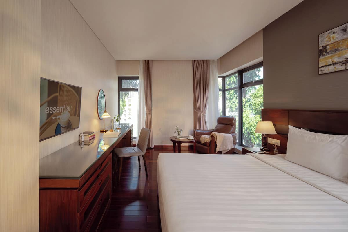 Een hotelkamer met een groot bed, een bureau met een stoel, een klein tafeltje en een raam met gordijnen.