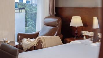 Ein Hotelzimmer mit einem Bett, einem Ledersessel, einem Nachttisch mit Lampen und Blick auf Gebäude durch das Fenster.