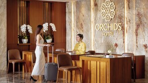 Un comptoir d’accueil avec un sol en marbre, des panneaux en bois et le logo de l’hôtel Orchids.