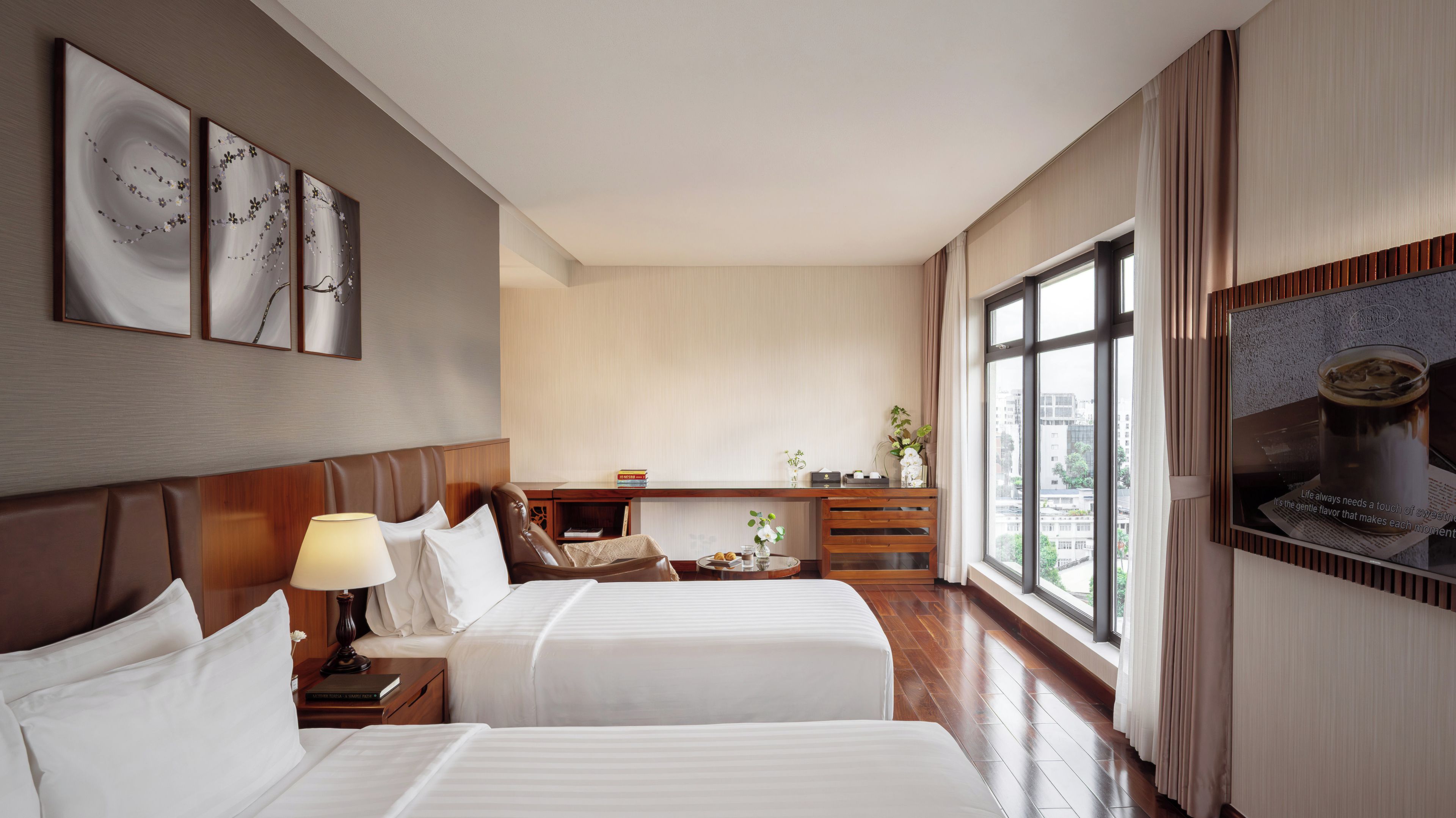 Habitación de hotel con dos camas, un escritorio, una silla, una lámpara y un ventanal con vistas.