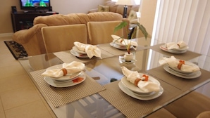 A dining table set with plates, napkins, and a vase of flowers in a modern living room with a sofa and a television in the background. - Ly53805 - Terrace Ridge - 4 Bed 2 Baths Condo (Davenport)