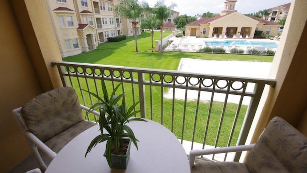 A balcony with a table and chairs, overlooking a pool and a well-maintained lawn with palm trees. - Ly53805 - Terrace Ridge - 4 Bed 2 Baths Condo (Davenport)