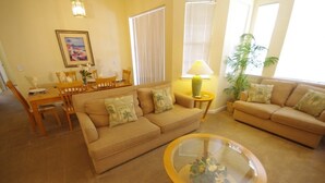 A living room with two beige sofas, a glass coffee table, a dining table with chairs, and a painting on the wall. - Ly53805 - Terrace Ridge - 4 Bed 2 Baths Condo (Davenport)