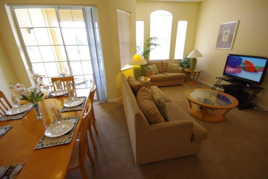A living room with a sofa, a coffee table, a TV, and a dining area with a table set for two.