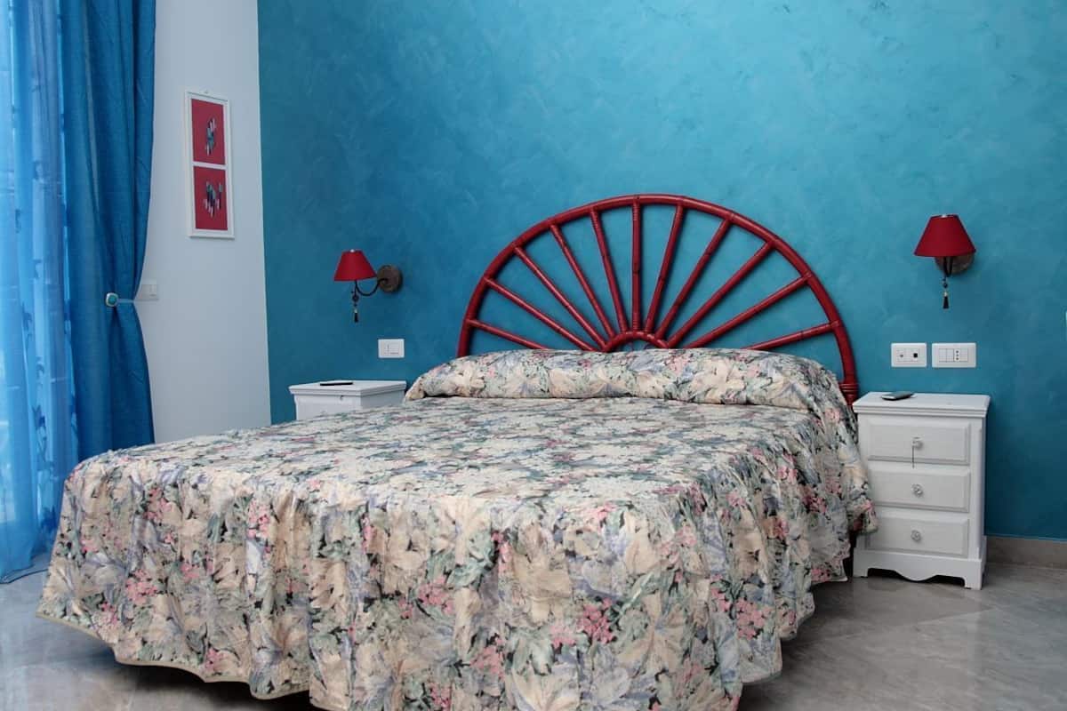 A bed with a floral bedspread, a red headboard, two bedside tables with lamps, and a blue wall.