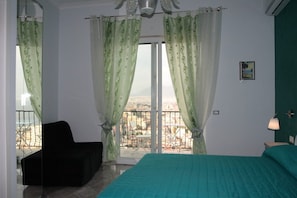 A bedroom with a bed, a chair, and a balcony with a view. - Nido Dei Gabbiani (Naples)