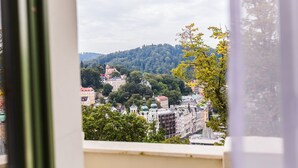 Une vue depuis une fenêtre donnant sur un paysage urbain, avec des bâtiments, des arbres et des collines.
