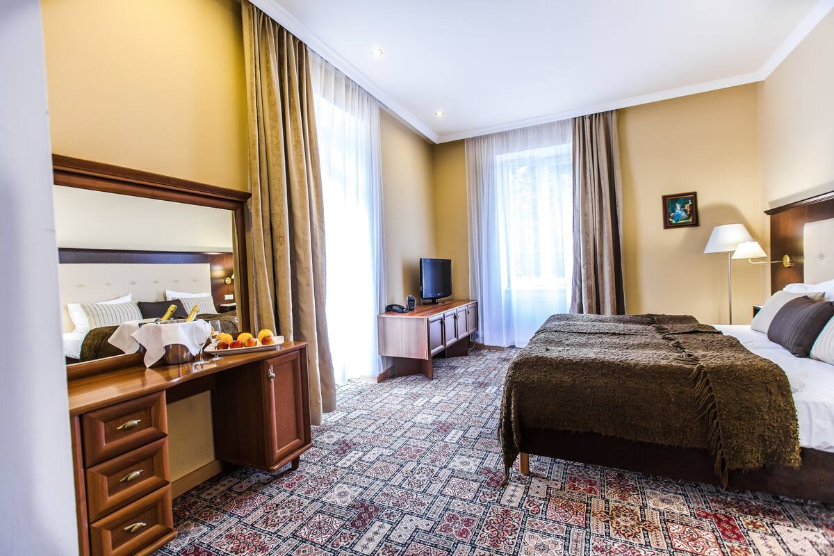 Een hotelkamer met een bed, een bureau met een computer, een televisie en een raam met gordijnen.
