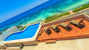 Ein Pool mit Holzterrasse und Liegestühlen mit Blick auf den Ozean.
