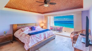 Ein Schlafzimmer mit hölzernem Kopfteil, einem Bett mit floraler Bettwäsche, einem Deckenventilator, einem Nachttisch, einem Fernseher und Meerblick.