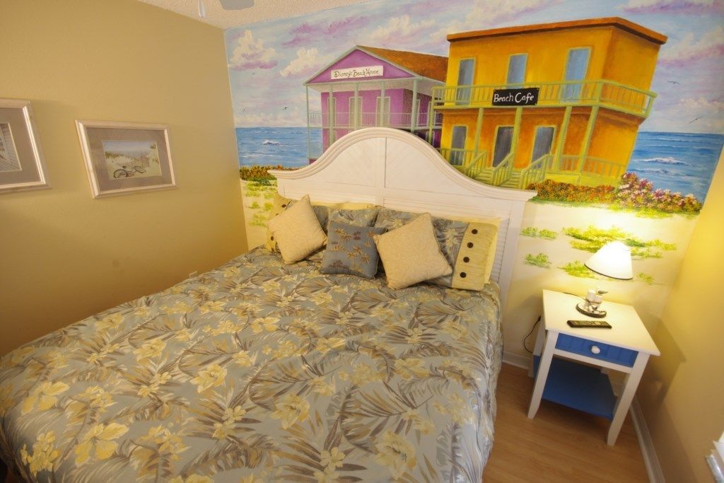 A bedroom with a bed, a nightstand, and a wall mural of a beach scene.