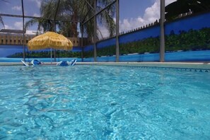 A swimming pool with clear water, lounge chairs, and a thatched umbrella.