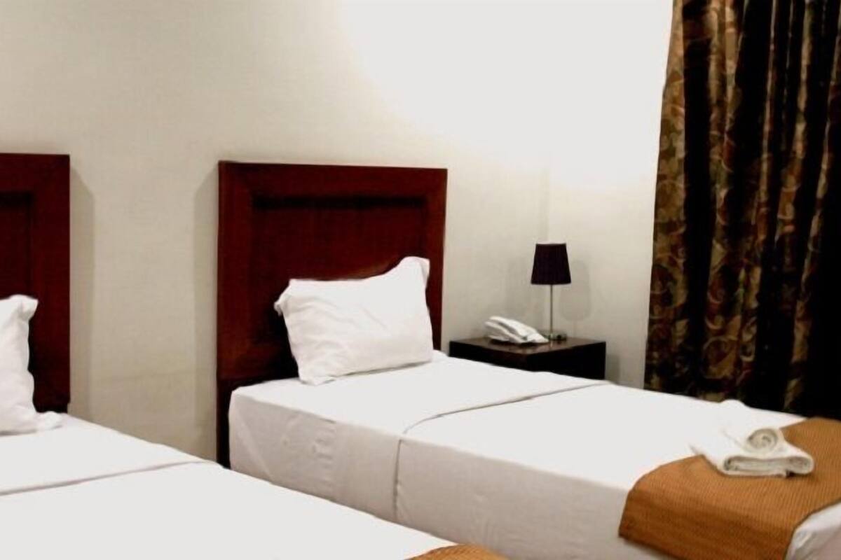 A hotel room with two single beds, a nightstand with a phone, and a curtain.