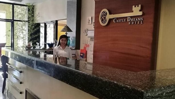 A reception desk at Castle Dreams Hotel with a key-shaped logo, a counter with a marble top, and a person standing behind it. - Castle Dreams Hotel (Davao)