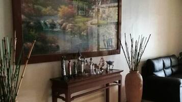 Un soggiorno con un grande dipinto di un paesaggio, un tavolino consolle in legno con oggetti decorativi, un divano in pelle nera e un'alta composizione floreale con rami.