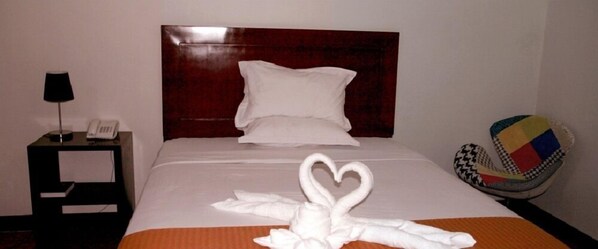 Una habitación de hotel con una cama bien hecha, un teléfono en la mesita de noche y una silla tejida de colores.