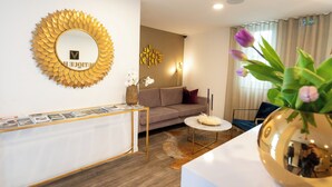 A modern living room with a round mirror, a sofa, a coffee table, and a decorative vase with flowers. - V Boutique Hotel (Boeblingen)