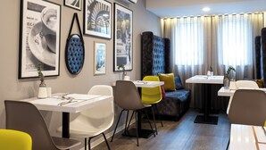 A modern hotel room with a dining area, a sofa, and a view of the city through large windows. - V Boutique Hotel (Boeblingen)