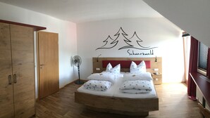 Un dormitorio con cama de madera, un ventilador de pie y una pared con diseño de bosque y montaña.