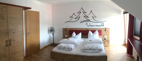 Un dormitorio con cama de madera, un ventilador de pie y una pared con diseño de bosque y montaña.