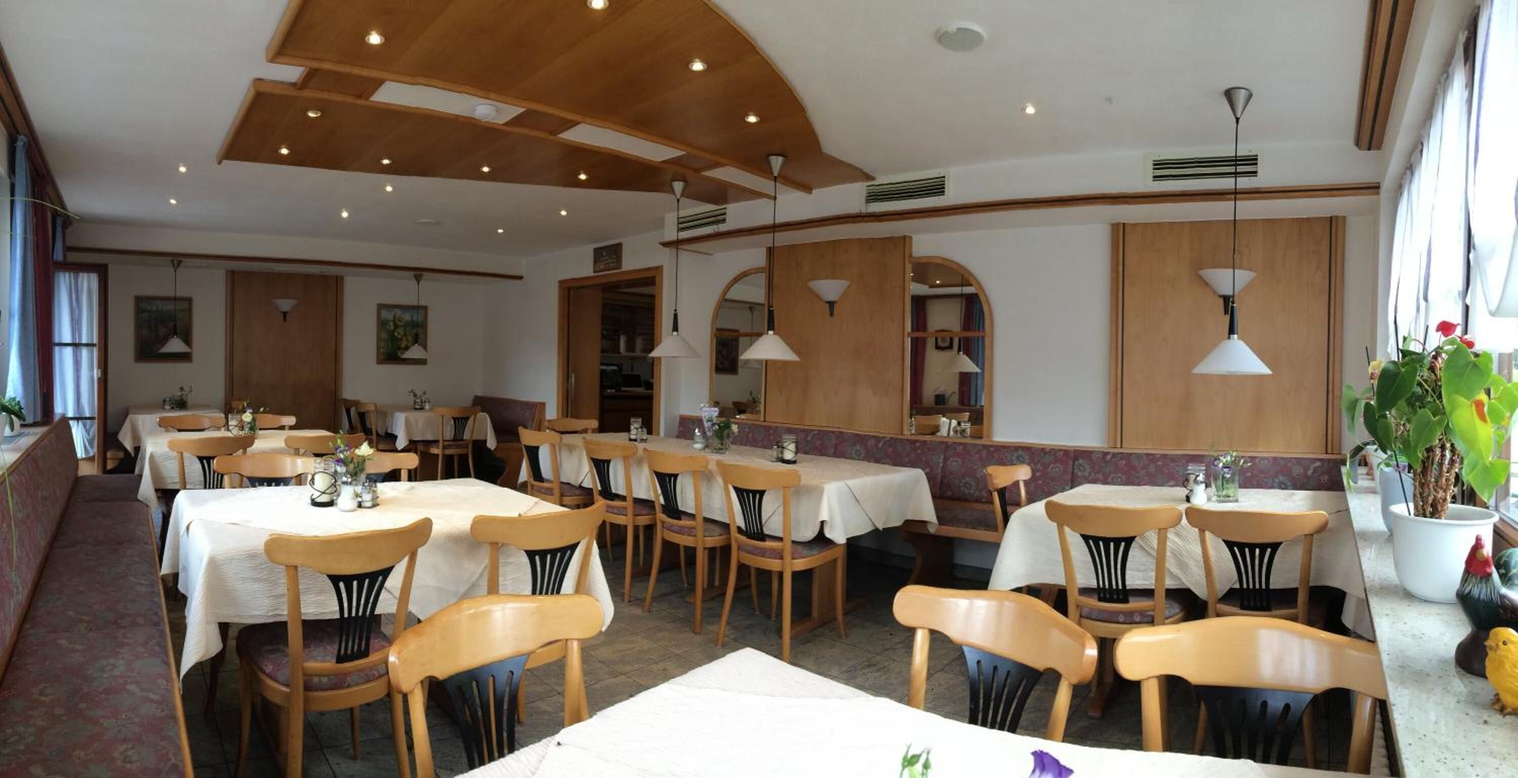 A restaurant with wooden tables and chairs, white tablecloths, and pendant lighting.
