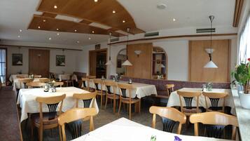 A restaurant with wooden tables and chairs, white tablecloths, and pendant lighting.