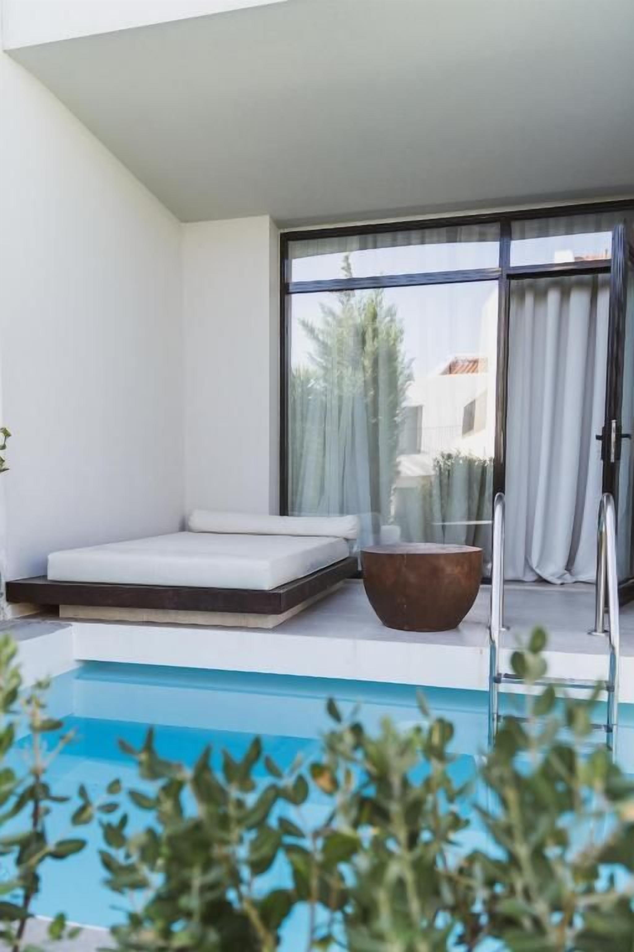 A modern outdoor pool area with a sun lounger, a seating area, and a view of the surrounding landscape.