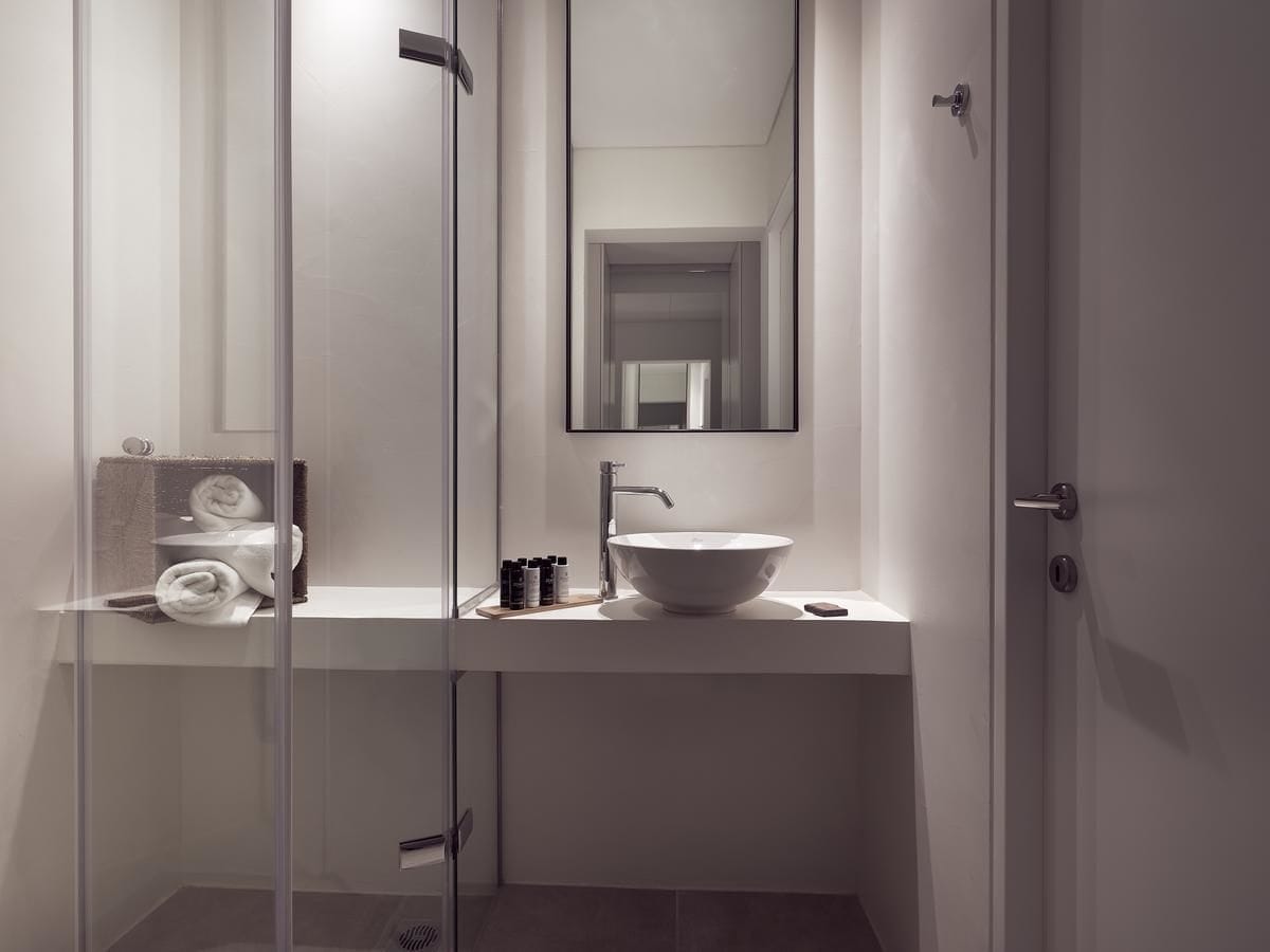 Un bagno moderno con box doccia in vetro, lavabo bianco con bacino a vista e specchio sopra il lavabo.